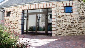 A building with a stone facade, large glass doors, and a brick pathway leading to the entrance. - Hôtel Auberge de la Loire (Mauges-sur-Loire)