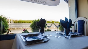 A table set for dining with a view of a river and greenery, a sign reading "Auberge de la Loire", and a window with a view of the landscape. - Hôtel Auberge de la Loire (Mauges-sur-Loire)