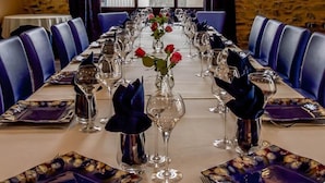 A dining room with a long table set for a meal, stone walls, and large windows. - Hôtel Auberge de la Loire (Mauges-sur-Loire)