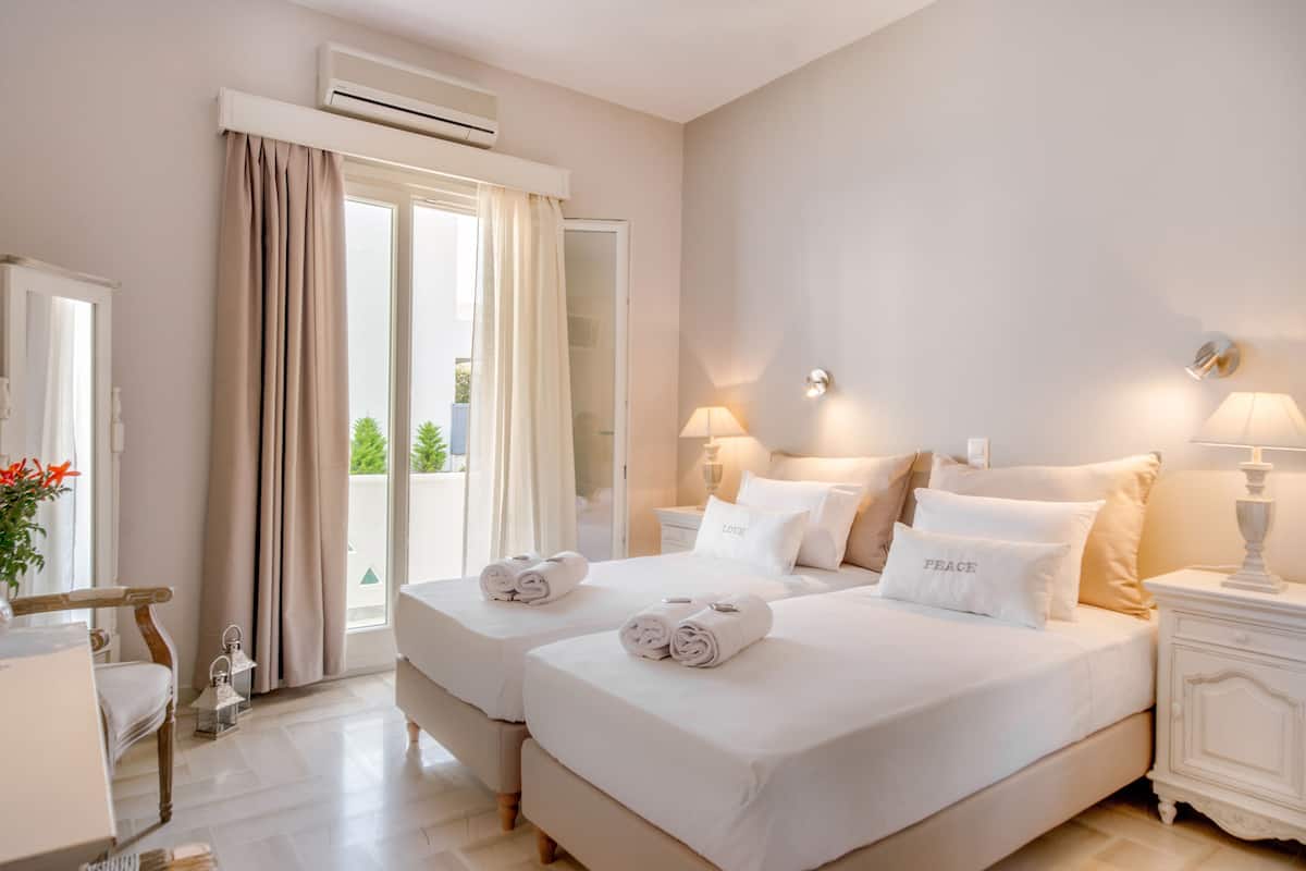 A hotel room with two beds, a sitting area, and a balcony with curtains.