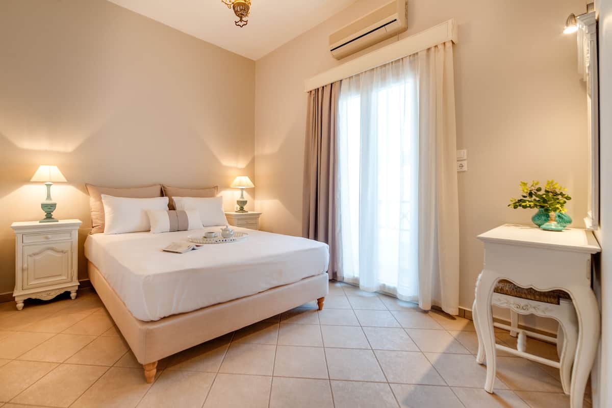 A neatly arranged bedroom with a large bed, bedside tables with lamps, a small side table with a vase, and a window with curtains.
