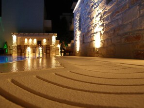 Un modelo de un edificio con zona de piscina, muros de piedra y una pequeña construcción con luces.