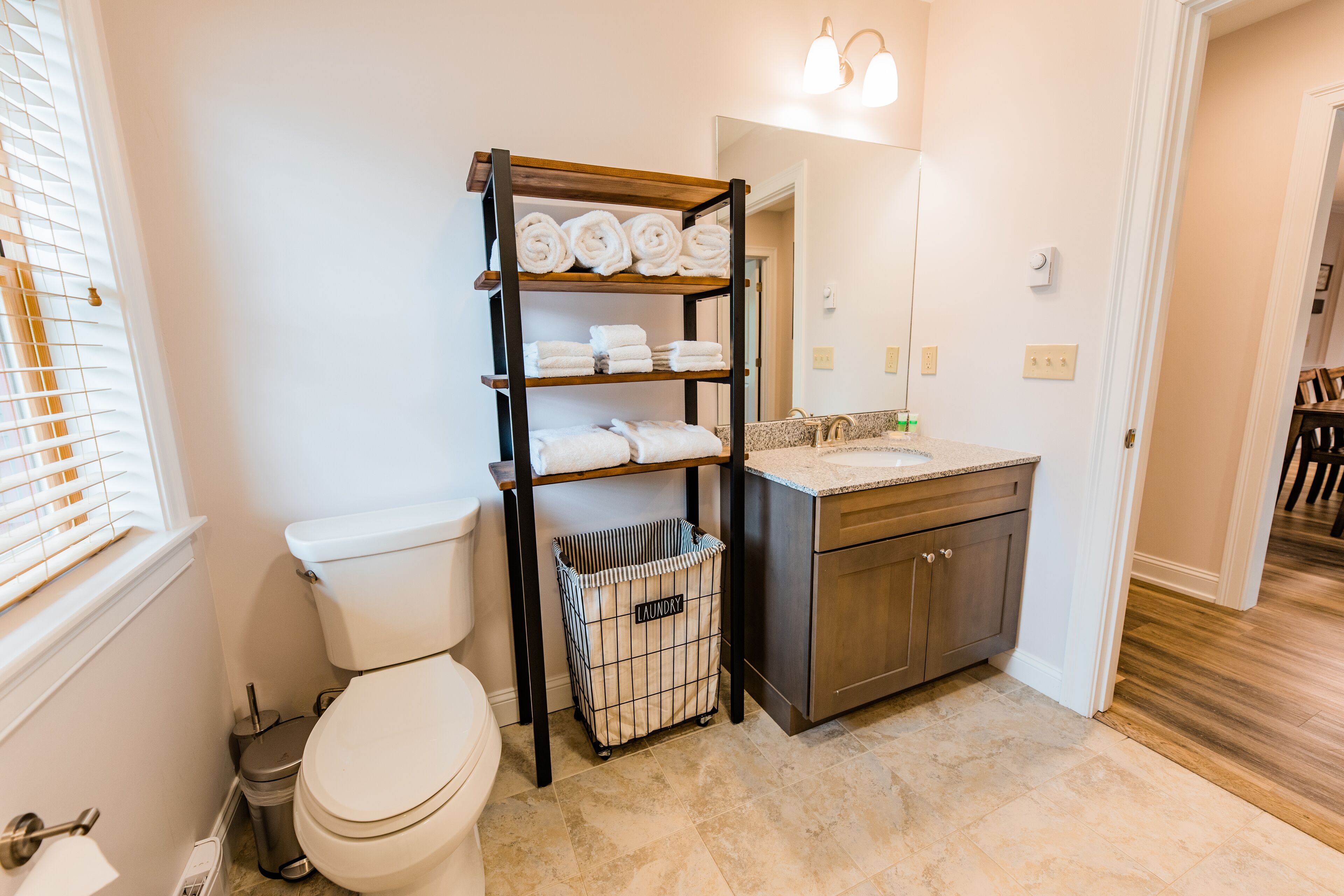 A bathroom with a toilet, a sink, a shelf with towels, and a laundry basket.