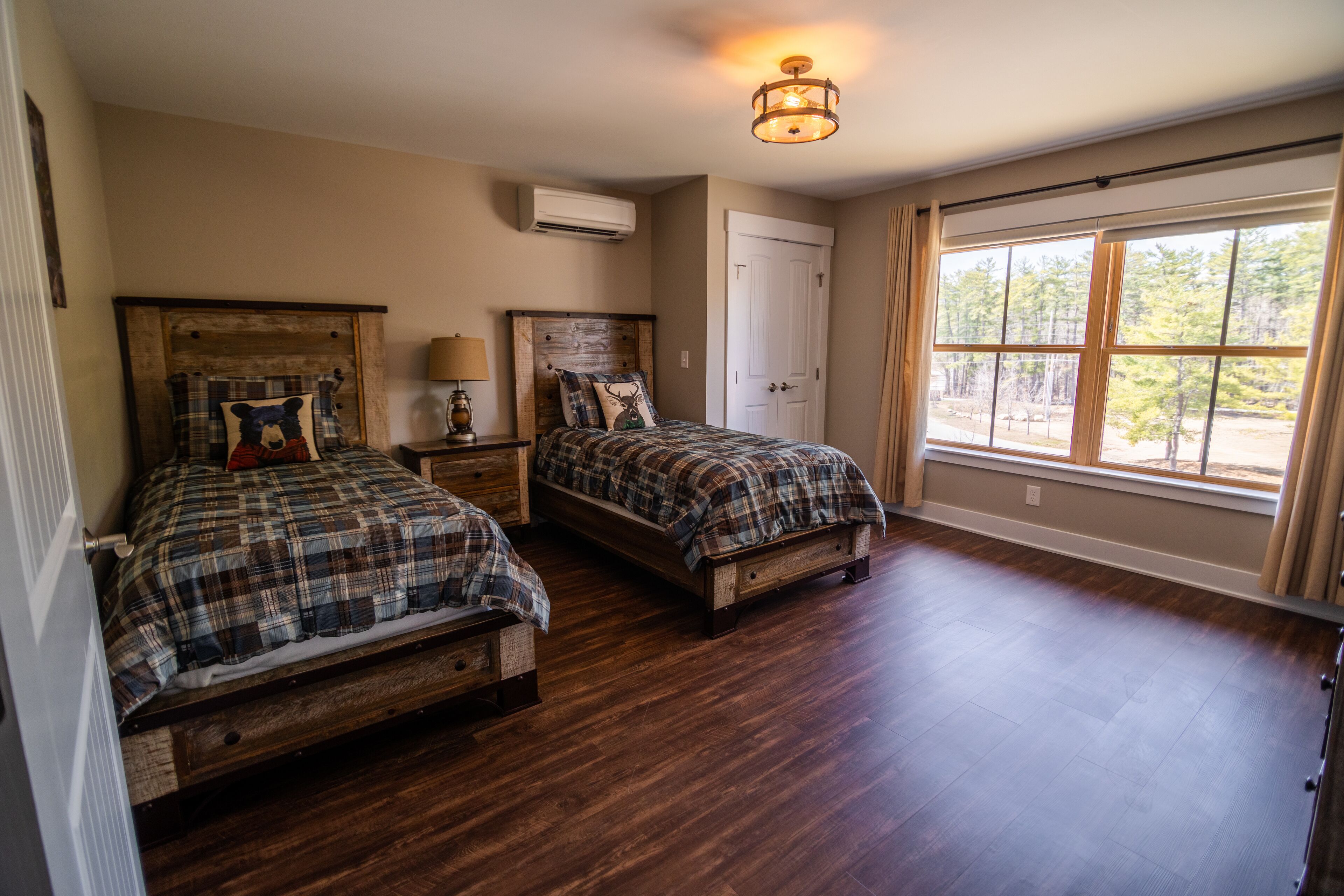 A bedroom with two wooden beds, a ceiling light fixture, an air conditioning unit, and a large window with curtains.