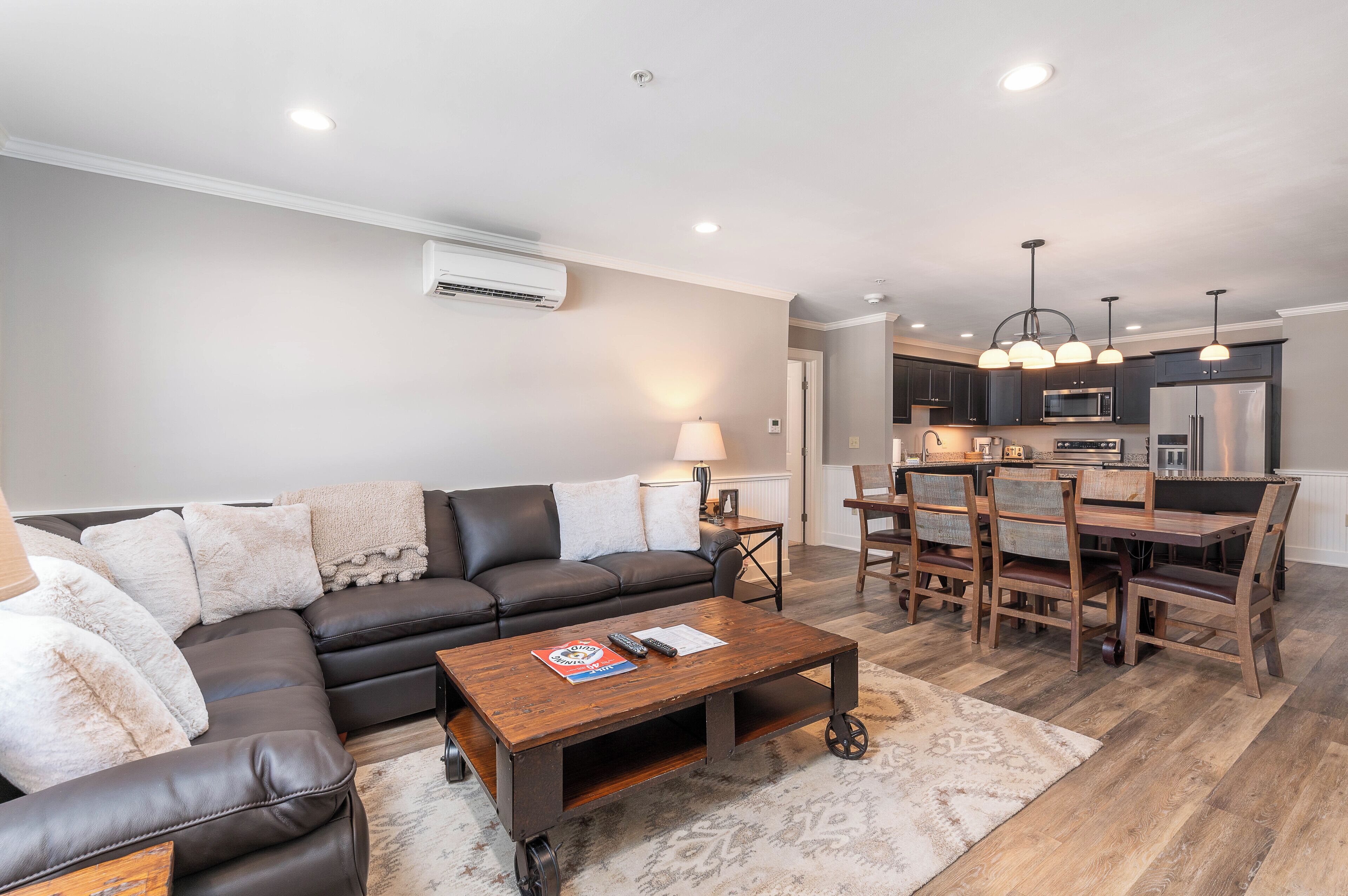 A modern living room with a sectional sofa, a coffee table, and a dining area with wooden chairs and a table.