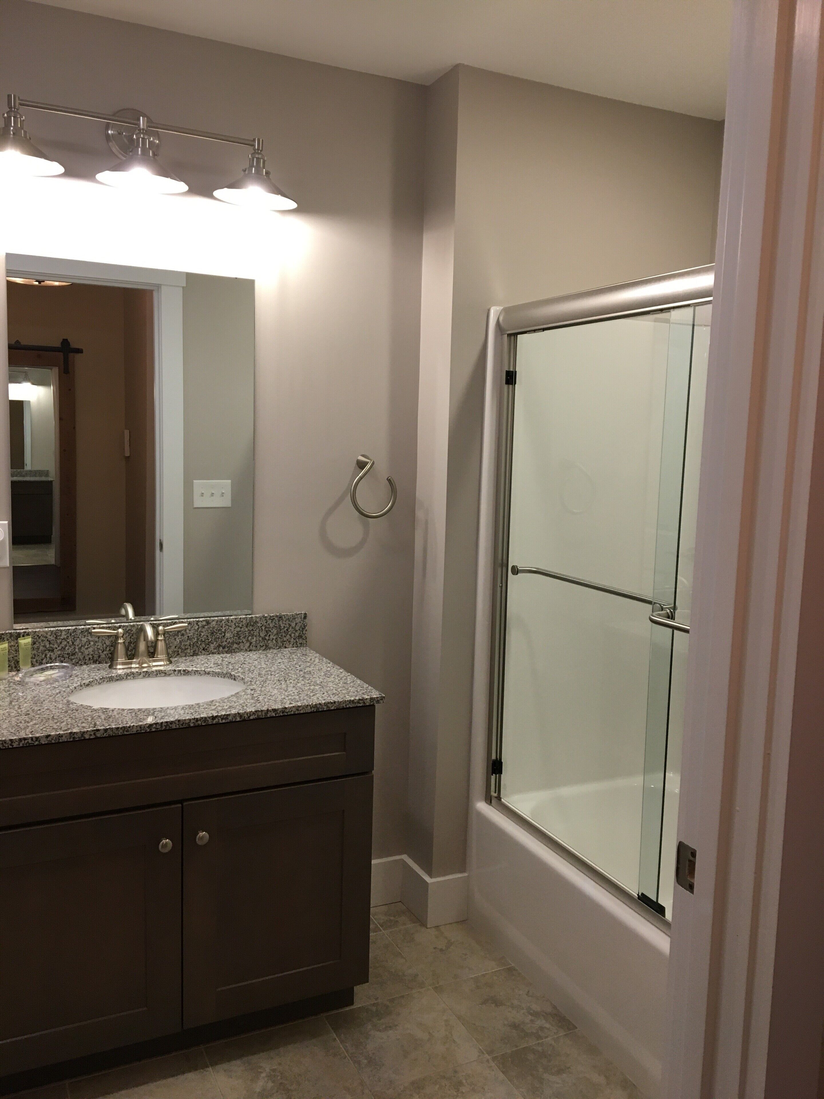 A bathroom with a granite countertop sink, a mirror, and a glass-enclosed shower.