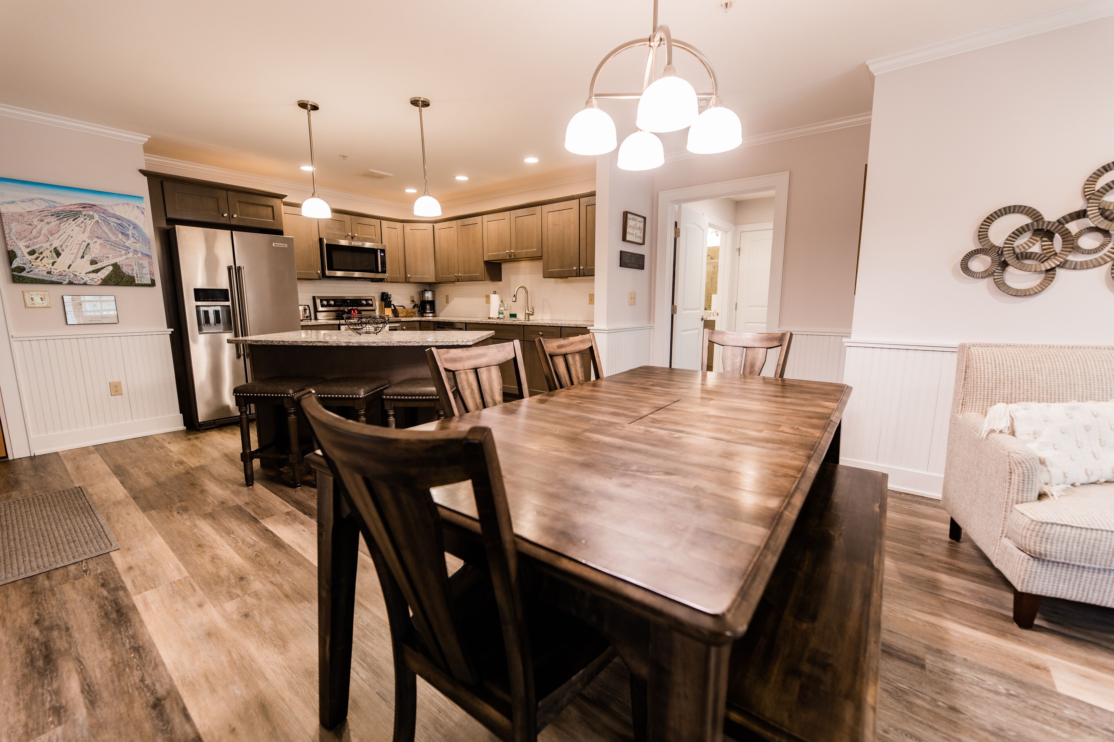 A spacious kitchen with a central island, wooden dining table, and chairs. There are pendant lights above the island and a microwave above the cabinets.