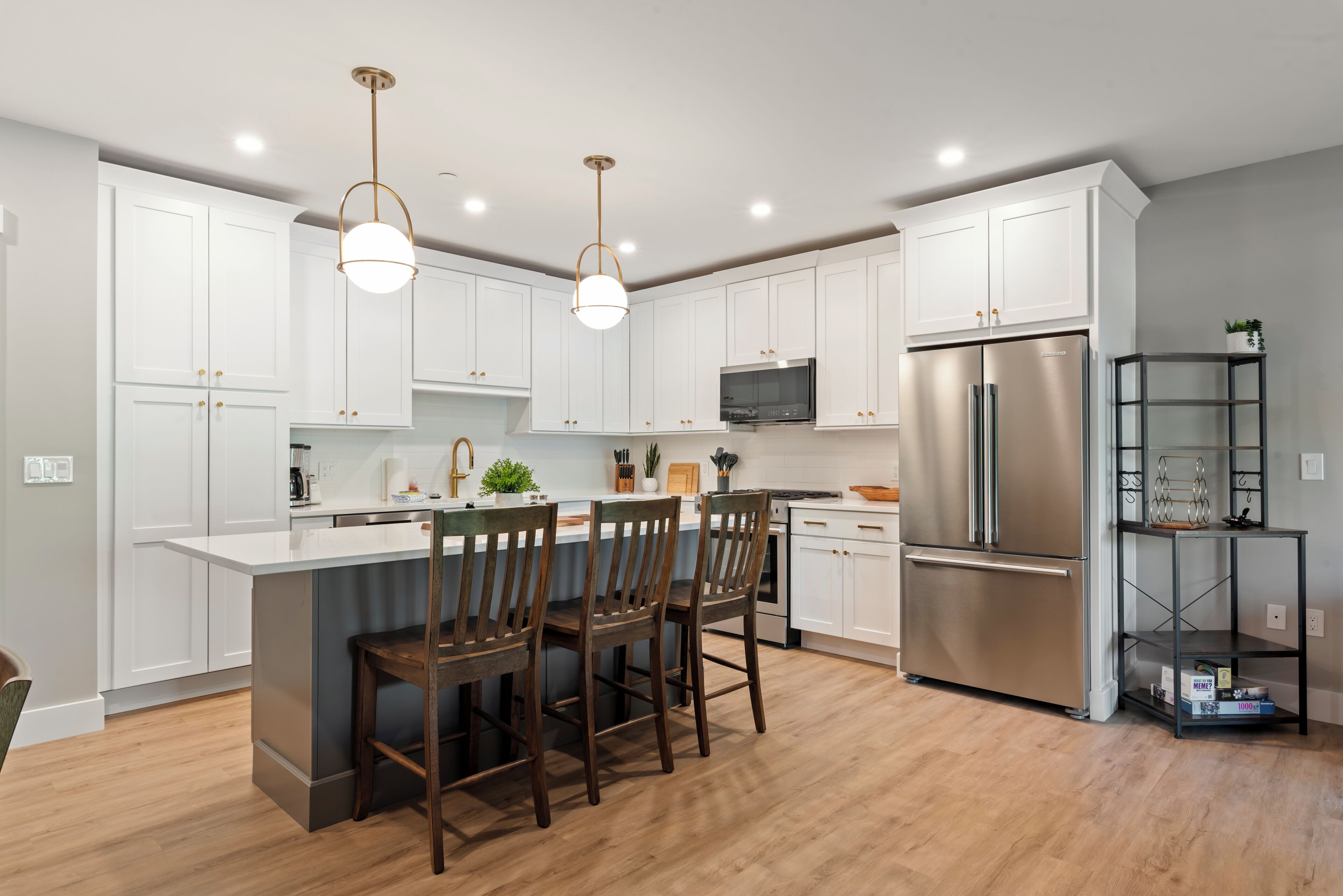 A modern kitchen with white cabinets, stainless steel appliances, and wooden chairs.