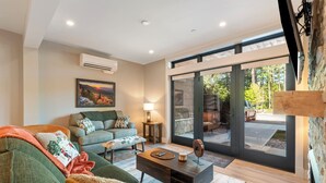 A modern living room with a sofa, coffee table, and a view of the outdoors through large glass doors. - Cranmore Condominium Lodging (North Conway)