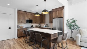 A modern kitchen with wooden cabinets, a large island with bar stools, stainless steel appliances, and pendant lighting. - Cranmore Condominium Lodging (North Conway)