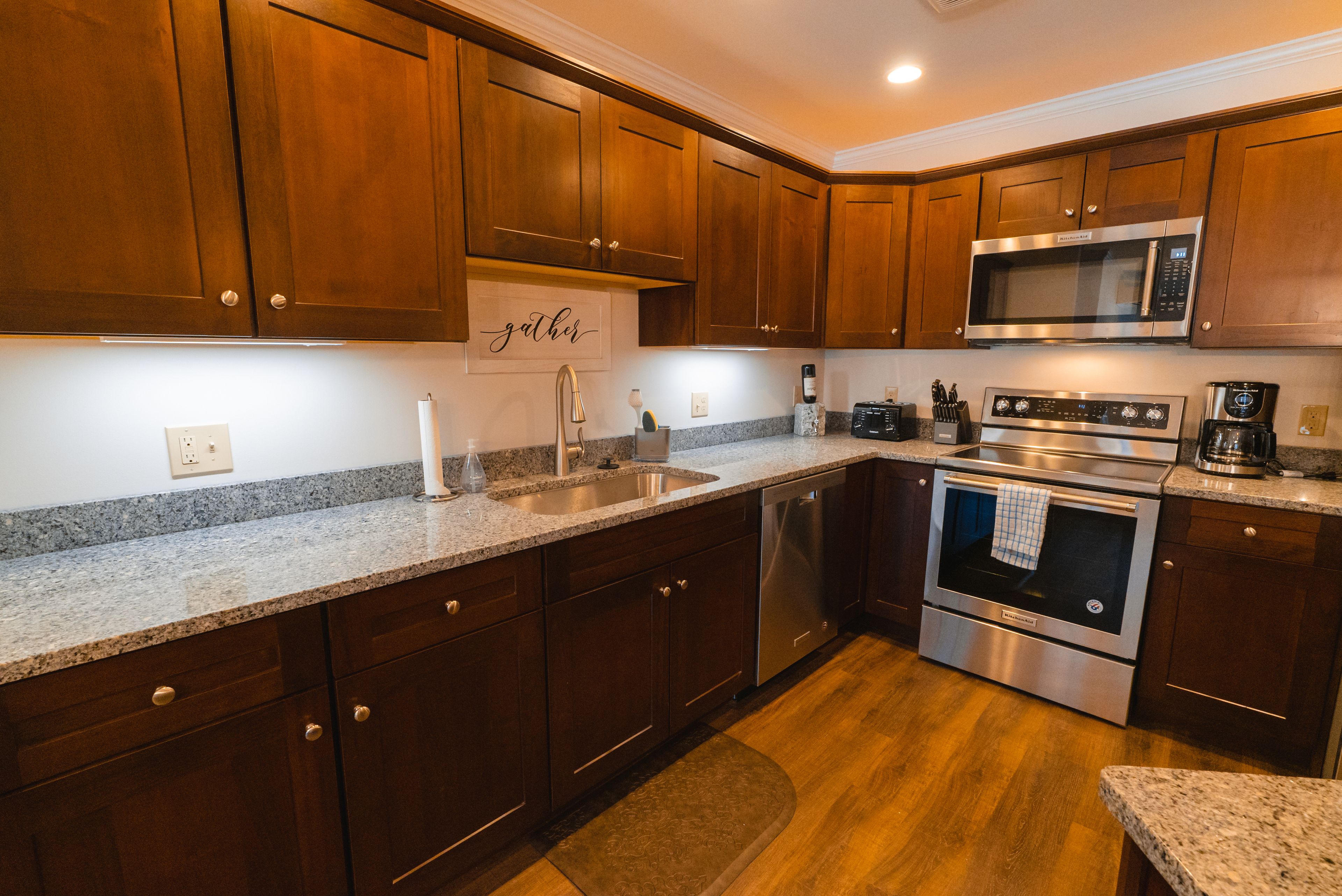 A kitchen with wooden cabinets, stainless steel appliances, granite countertops, and a granite backsplash.
