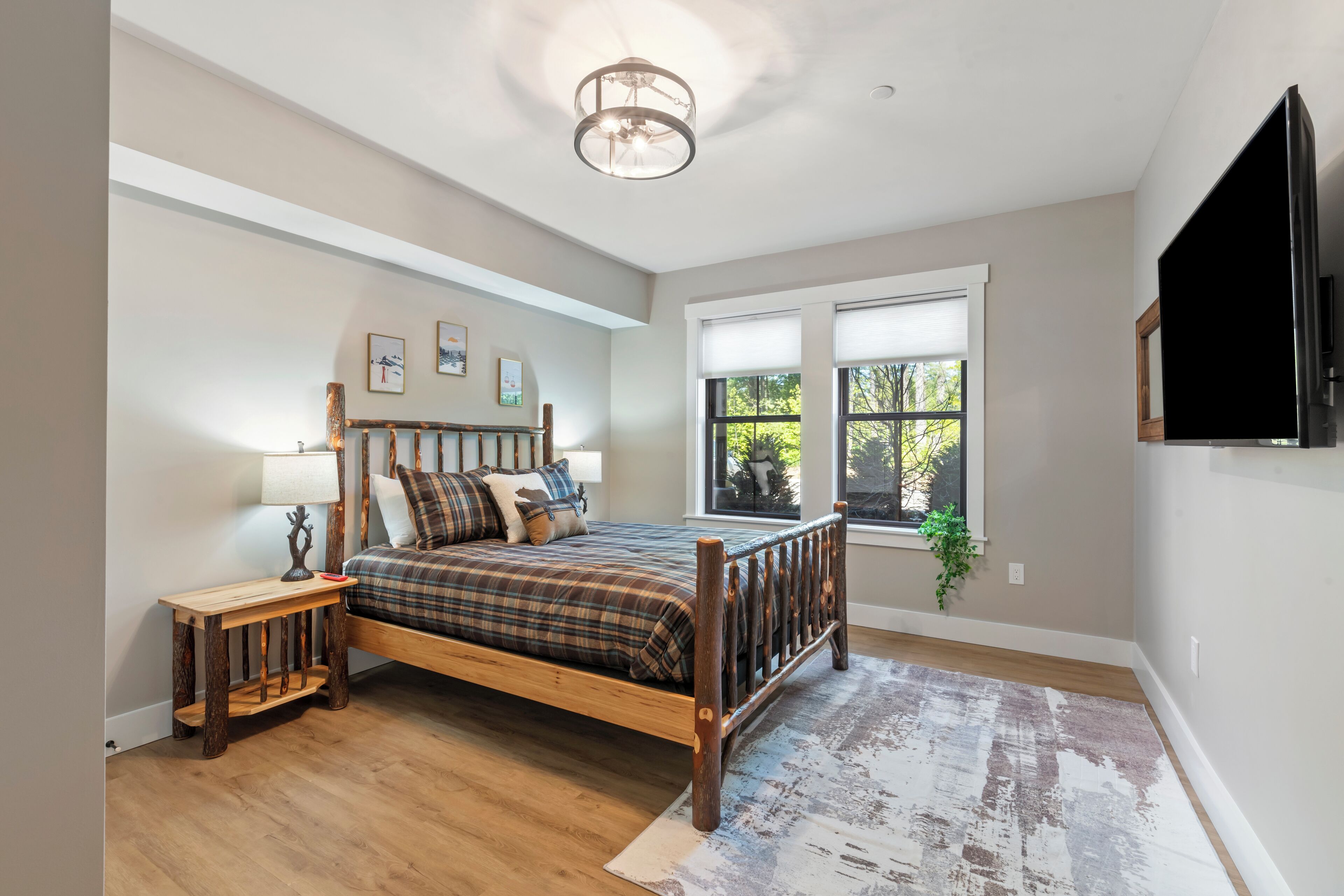 Une chambre à coucher avec un lit en bois, une table de chevet, une lampe, une fenêtre avec des stores et un luminaire au plafond.
