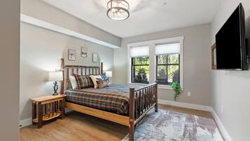 Une chambre à coucher avec un lit en bois, une table de chevet, une lampe, une fenêtre avec des stores et un luminaire au plafond.