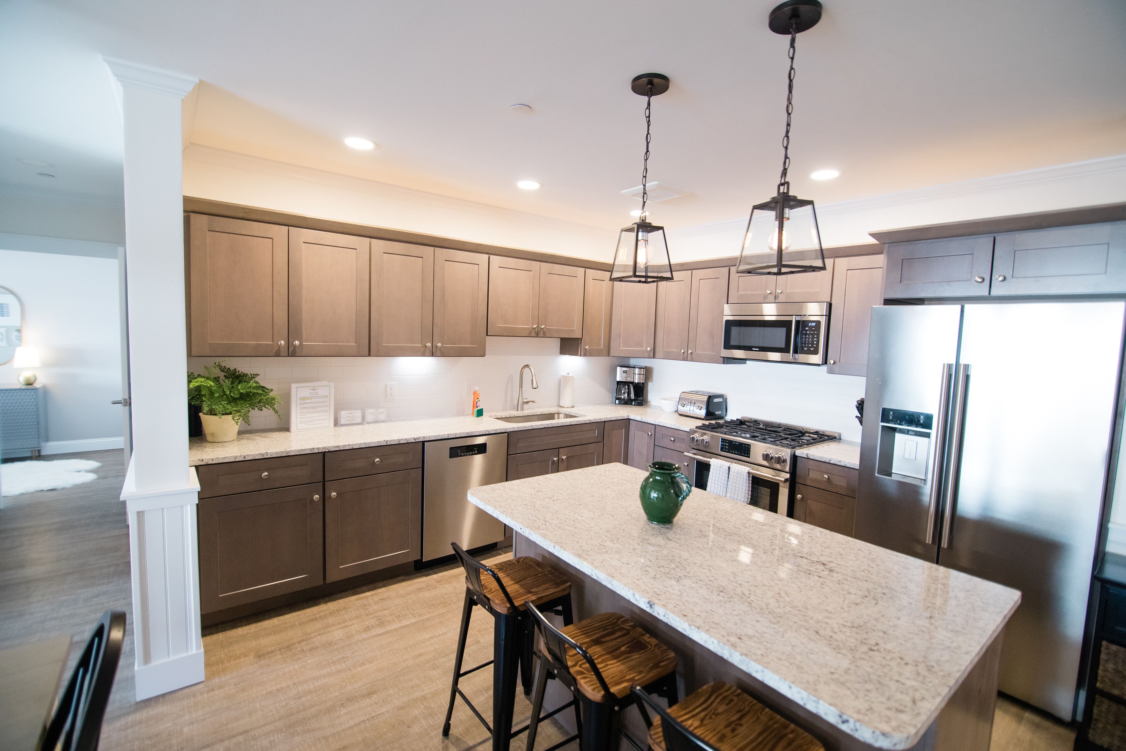 A modern kitchen with wooden cabinets, stainless steel appliances, a granite countertop, and a central island with bar stools.