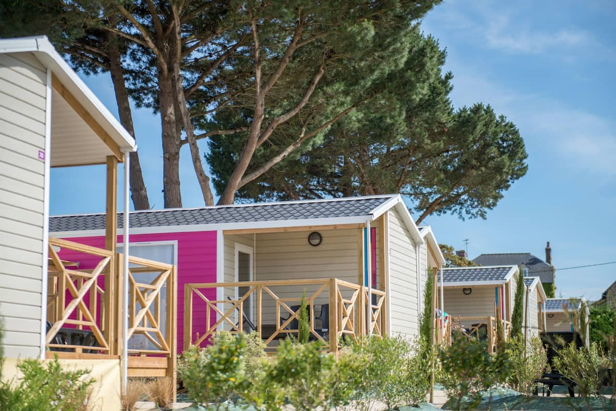 Une rangée de maisons mobiles dotées de terrasses en bois, entourées d’arbres et de verdure.