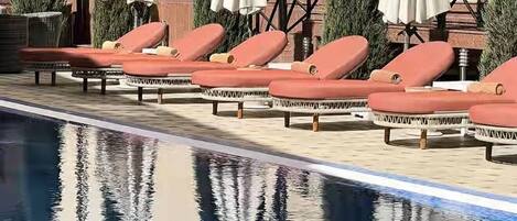 A poolside area with lounge chairs and umbrellas, a clear pool, and a building with a balcony.