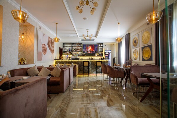 A bar area with a polished marble floor, leather seating, and a bar counter with a television screen displaying a fireplace.
