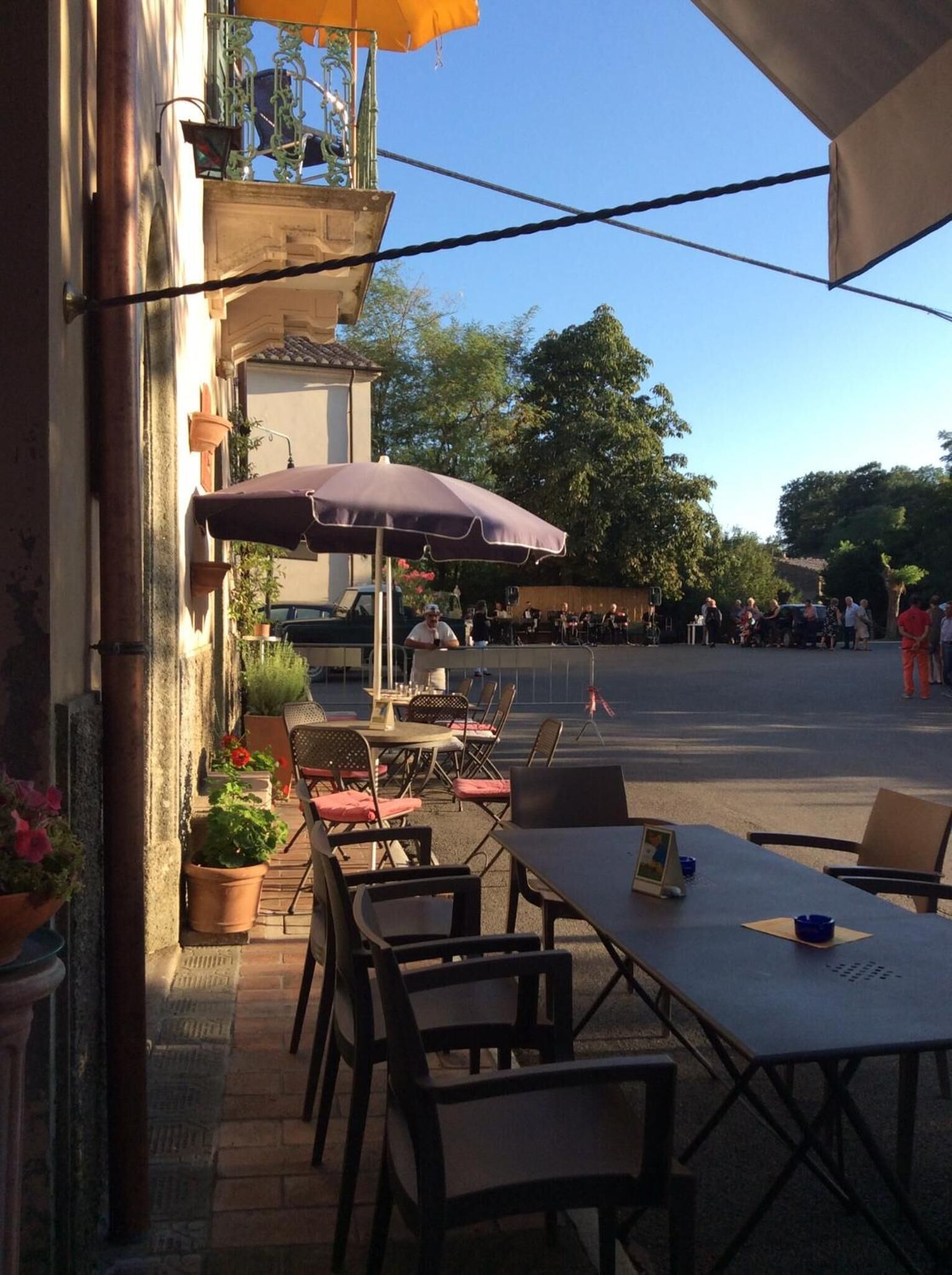 An outdoor café with tables and chairs, surrounded by potted plants and umbrellas.