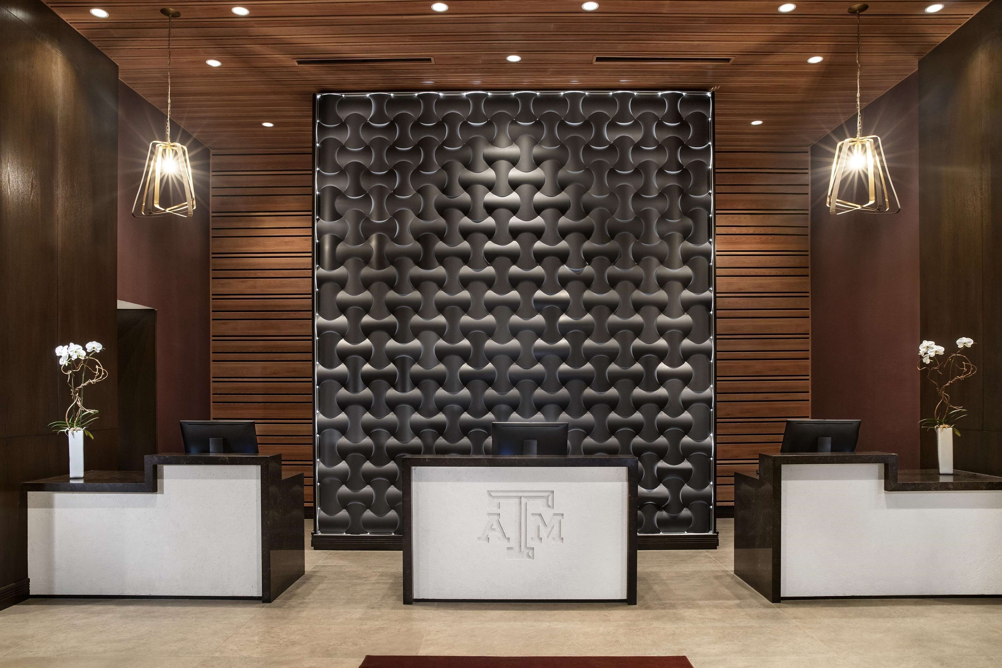 A reception area with a modern design, featuring a textured wall, two reception desks, and pendant lighting.
