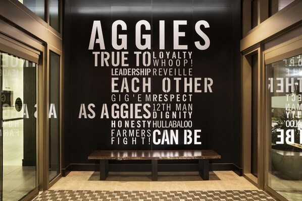 A wall with motivational text and a bench in a lobby area. - Texas A&M Hotel and Conference Center (College Station)