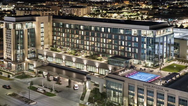 A modern hotel with a spacious outdoor pool, well-lit parking area, and a prominent entrance. - Texas A&M Hotel and Conference Center (College Station)