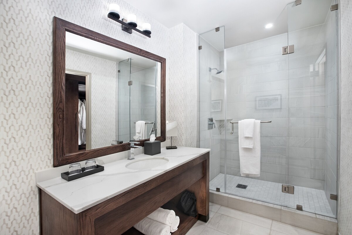 A modern bathroom with a large mirror, a sink, and a glass-enclosed shower.