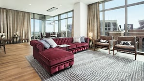 A spacious living room with a large window, a red velvet sofa, a patterned rug, and a view of a stadium. - Texas A&M Hotel and Conference Center (College Station)