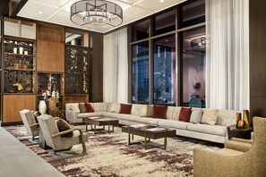A modern living room with a sectional sofa, armchairs, a coffee table, and a bookshelf. - Texas A&M Hotel and Conference Center (College Station)