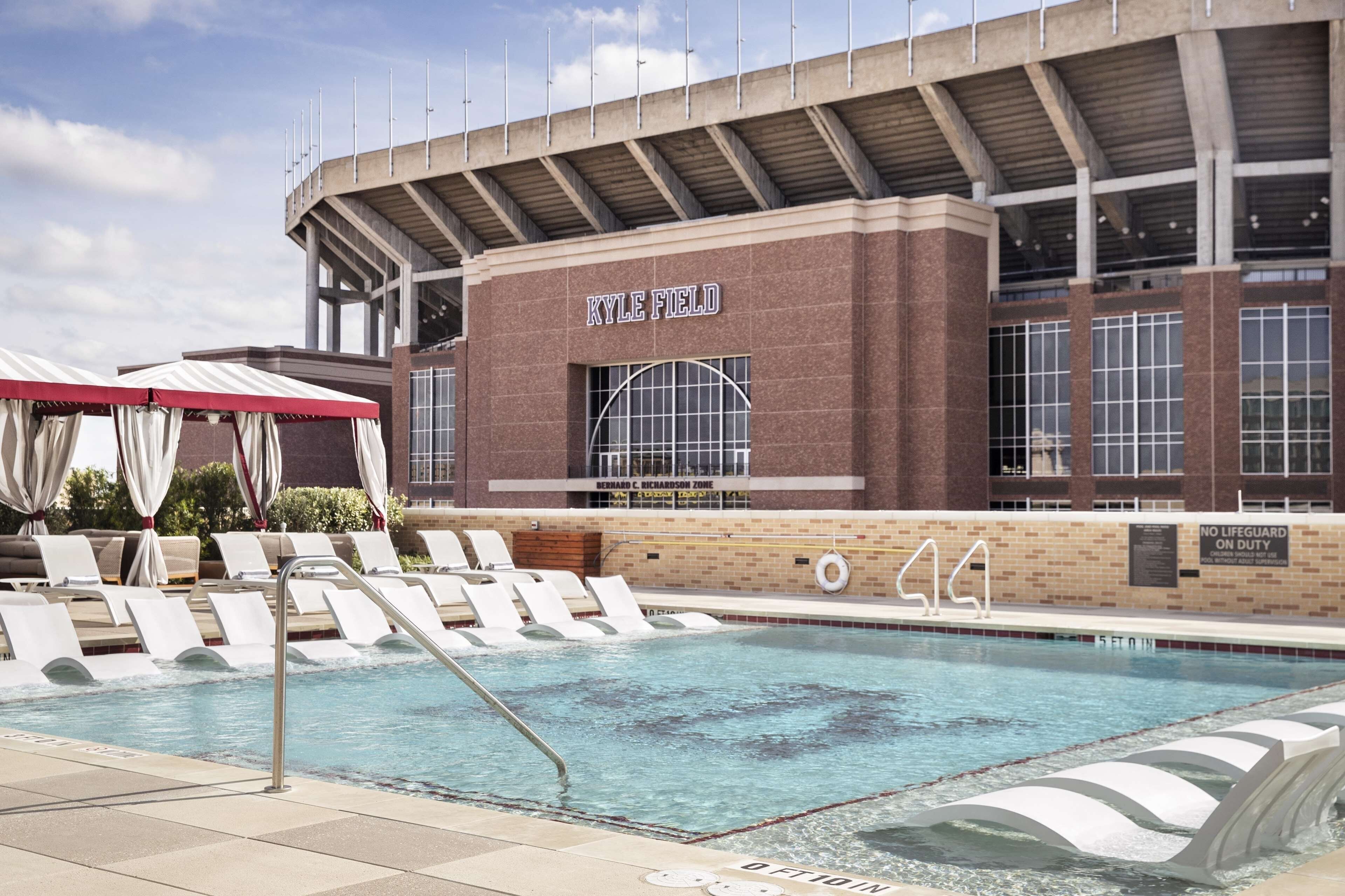 A swimming pool area with lounge chairs and a building labeled 'KYLE FIELD' in the background.