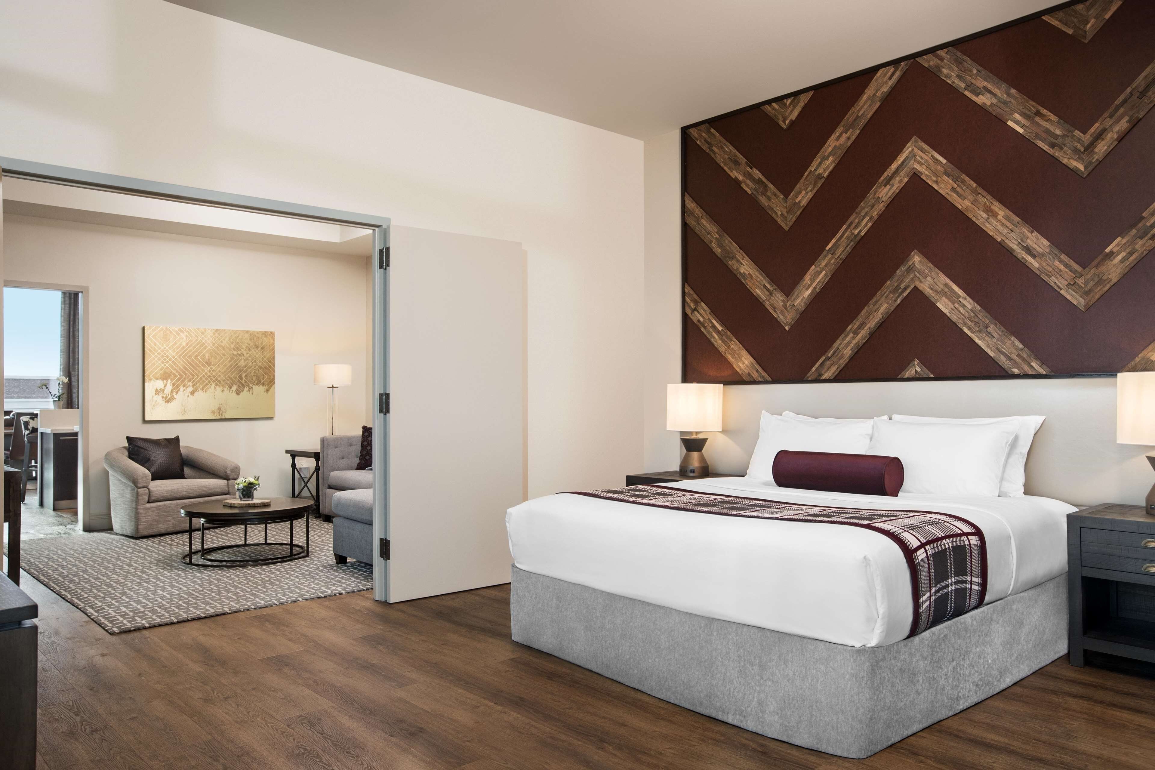 Habitación de hotel con cama, zona de estar con sofá y sillones, mesa de comedor y una pared grande con diseño de chevron.