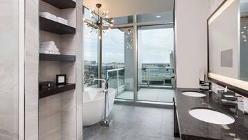 A modern bathroom with a freestanding bathtub, a large mirror, and a city view through the glass door.