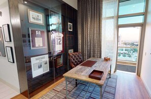 A room with a large window, a glass display case with memorabilia, a leather chair, and a wooden table. - Texas A&M Hotel and Conference Center (College Station)