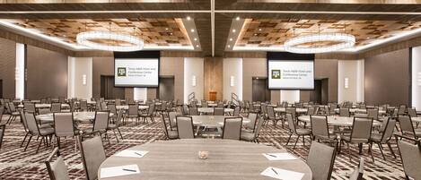 A conference room with round tables, chairs, and presentation screens.