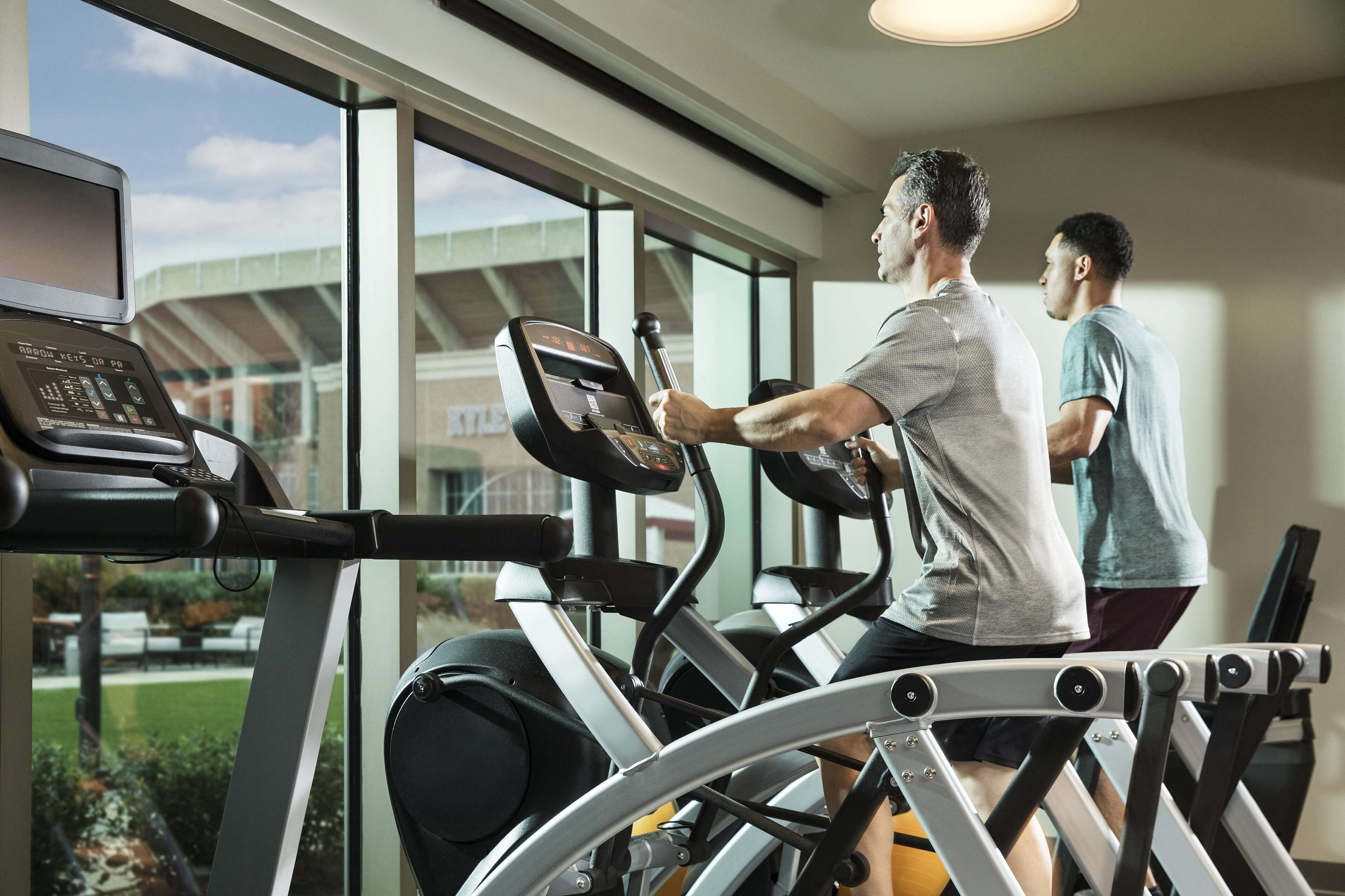 A gym with treadmills and a stationary bike, large windows, and a view of a building outside.