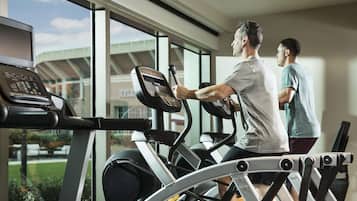 A gym with treadmills and a stationary bike, large windows, and a view of a building outside.