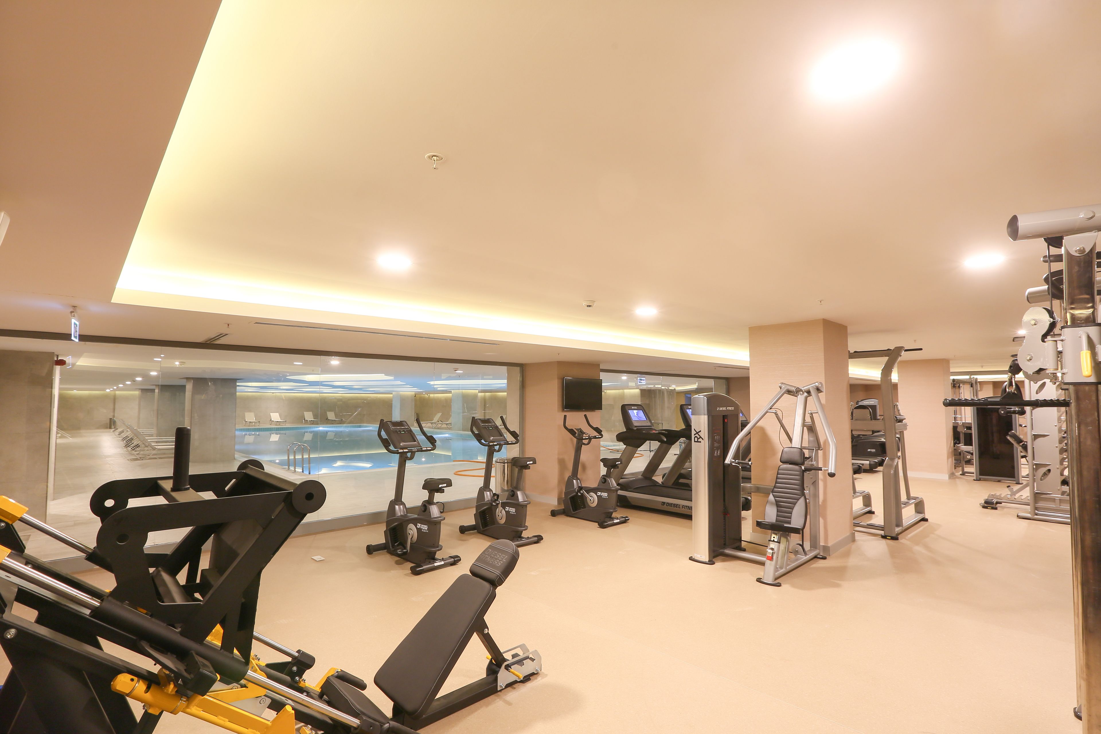 Un gimnasio bien iluminado con diferentes equipos de ejercicio, incluyendo cintas de correr, bicicletas estáticas y máquinas de pesas.