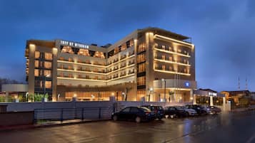 A modern hotel with multiple floors, a parking lot, and a well-lit facade.