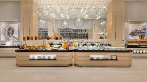Un espace buffet proposant différents stands de nourriture, notamment des fruits, des salades et des boissons.