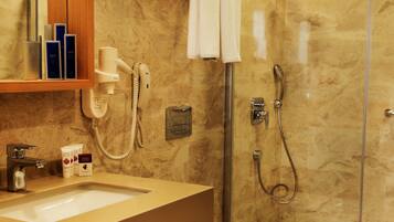 Un baño moderno con pared de mármol, ducha envuelta en vidrio, inodoro y tocador con lavamanos y perchero.
