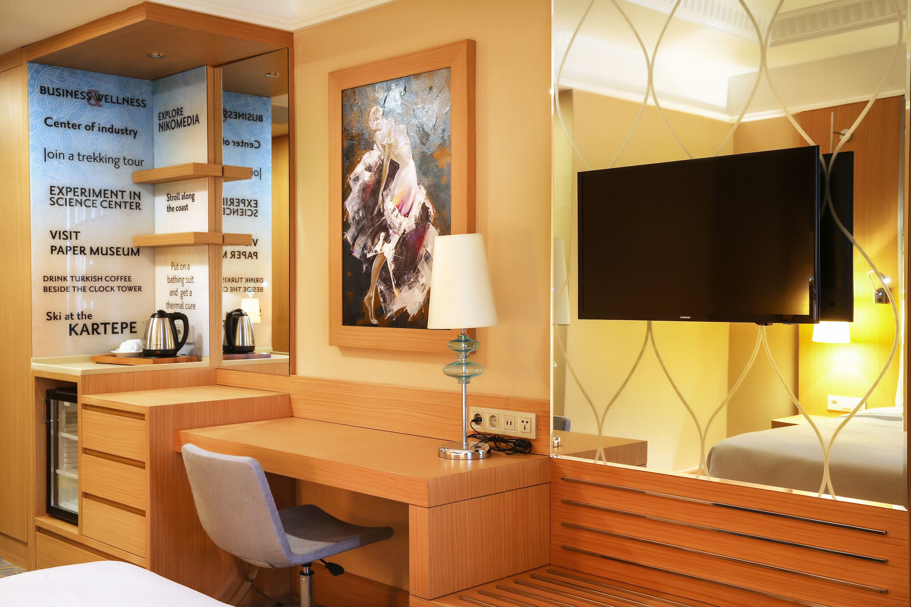 A hotel room with a wooden desk, a chair, a television, and a painting on the wall.