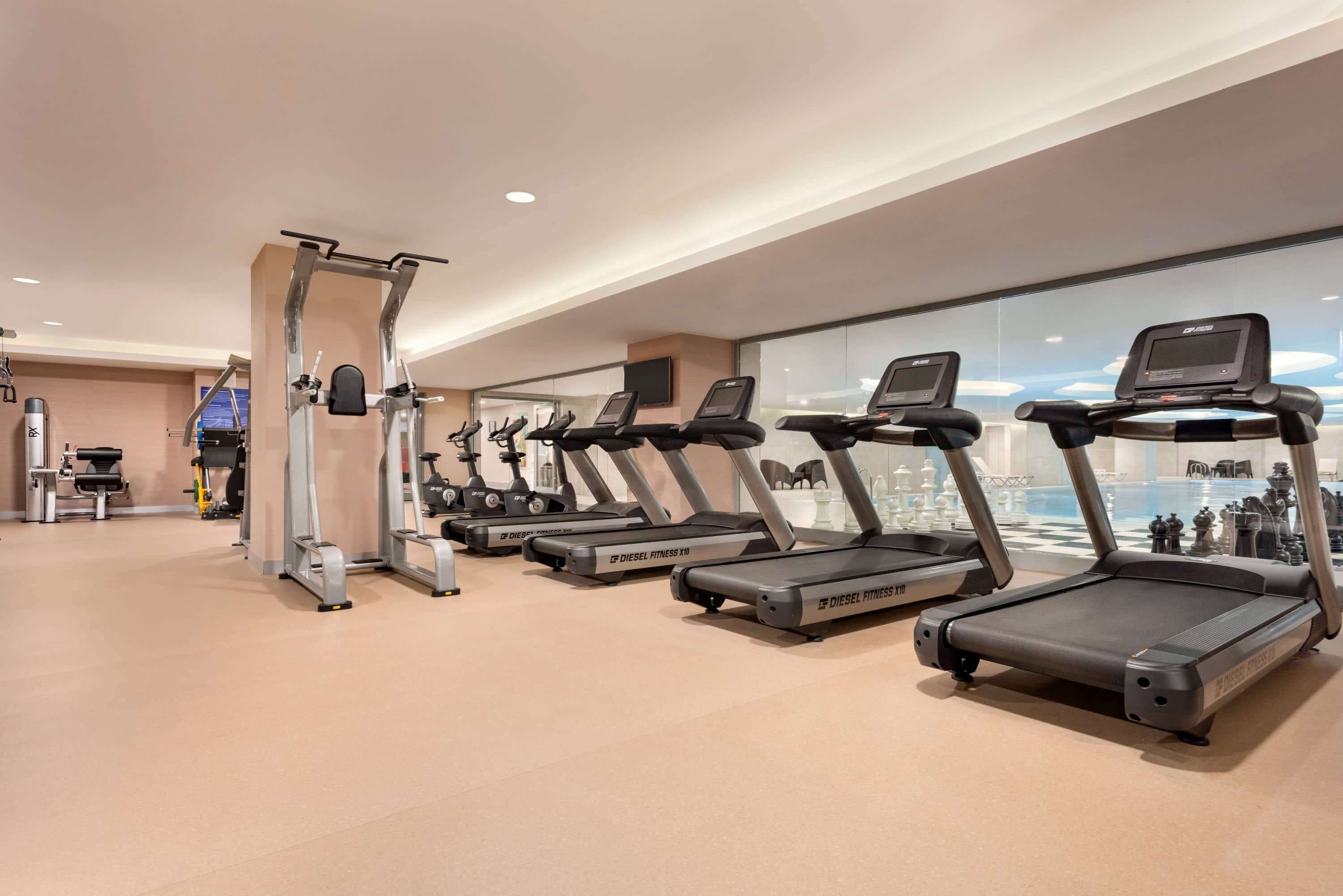Une salle de sport équipée de plusieurs tapis de course, d’une machine de musculation et d’une grande fenêtre donnant sur la ville.