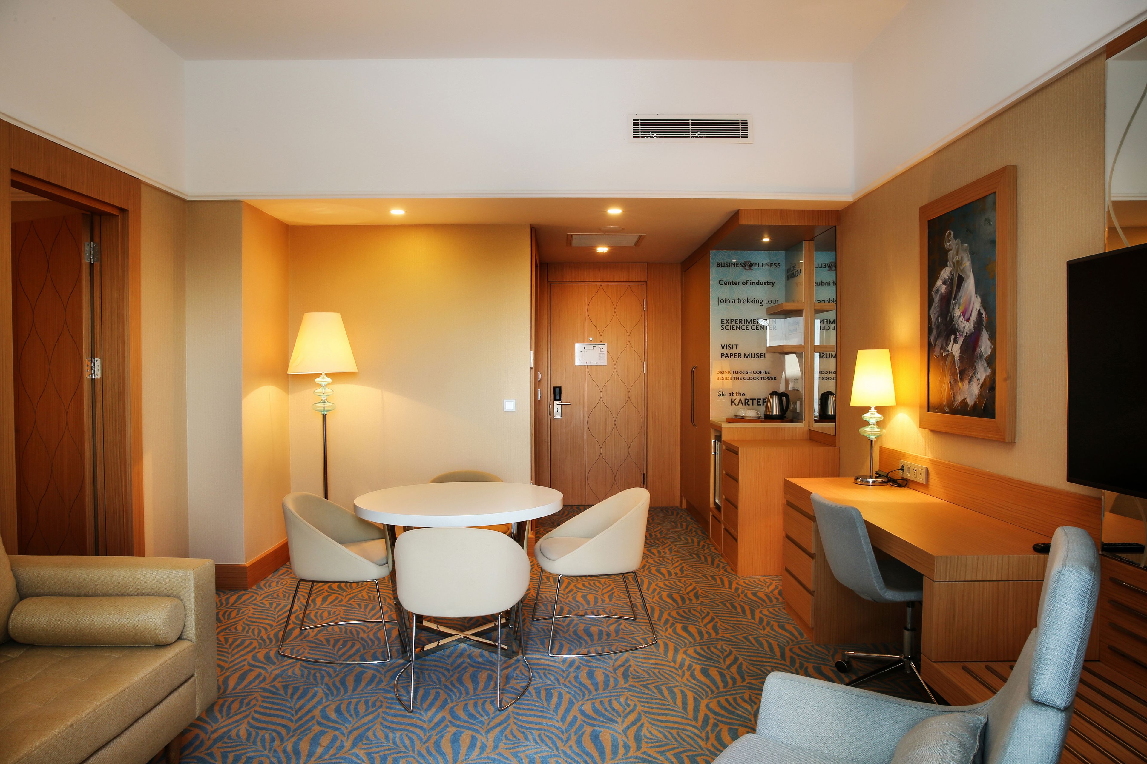 Habitación de hotel con una mesa de comedor, dos sillas, un sofá, un escritorio con una silla, un televisor y un cuadro en la pared.
