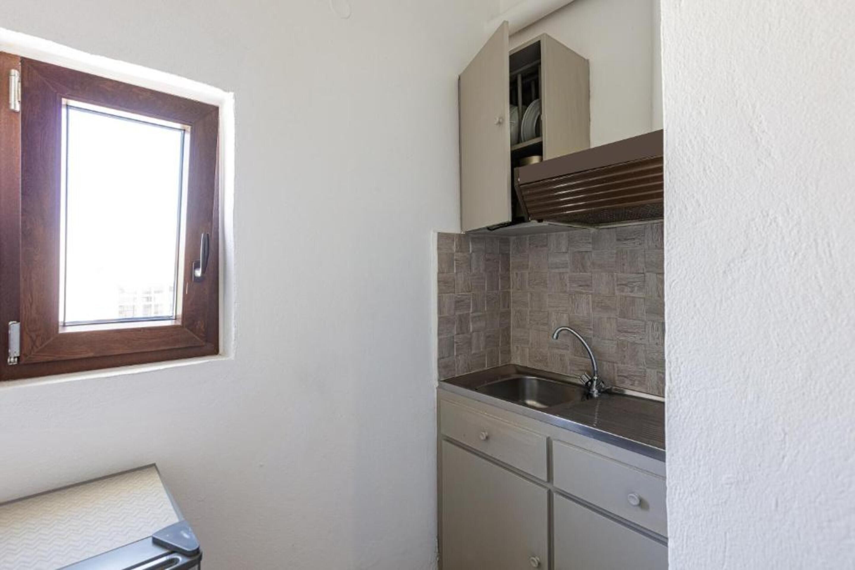 A compact kitchen with a window, a built-in sink, and a cabinet above the countertop.