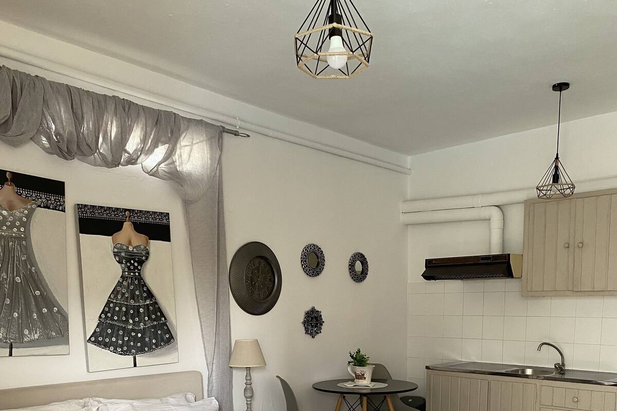 Ein Schlafzimmer mit einem Bett, einem Nachttisch, einer Lampe und einem Stuhl. Ein kleiner Tisch mit Pflanze und ein Spiegel an der Wand sind ebenfalls vorhanden.