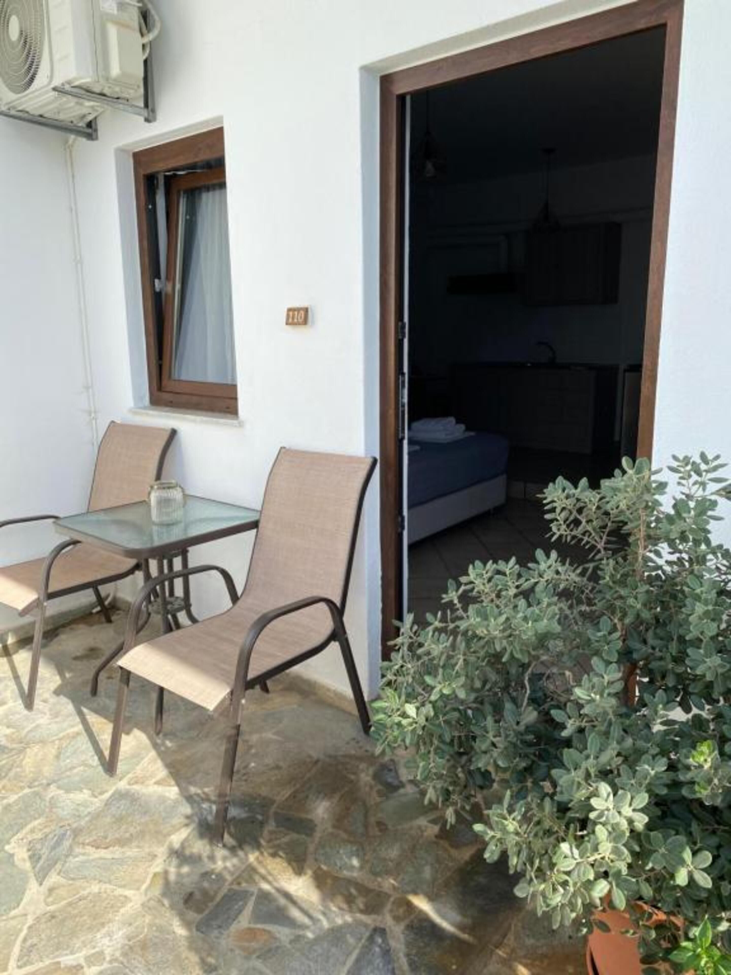 Une pièce avec une table et des chaises en verre, une plante en pot et une vue sur la cuisine.