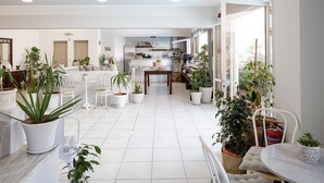 Amplia sala de estar con una cocina al fondo, piso de baldosas blancas y varias plantas en macetas.