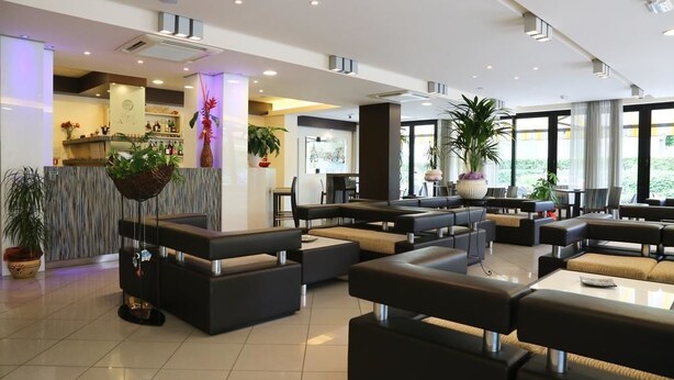 A modern hotel lobby with a reception desk, seating areas, and large windows. - Hotel Ambra (Cesenatico)