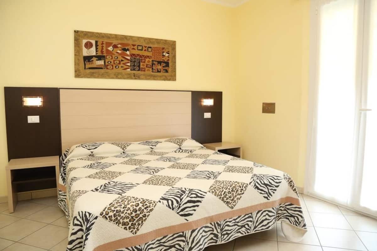 Un dormitorio con edredón estampado de cebra, cabecera con iluminación integrada y una obra de arte abstracto colgada en la pared.