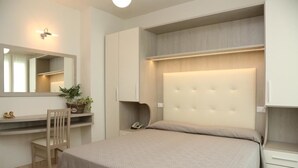 A bedroom with a bed, a desk, a chair, a mirror, and a bedside table. - Hotel Ambra (Cesenatico)