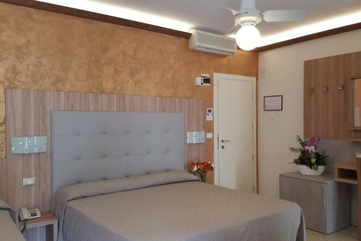Un dormitorio con una cama grande, un escritorio, una silla, un espejo y una planta pequeña.